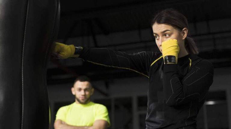 defensa-personal-vista-lateral-boxeadora-guantes-proteccion-perforando-saco-pesado-focus-0.39-0.61-896-504